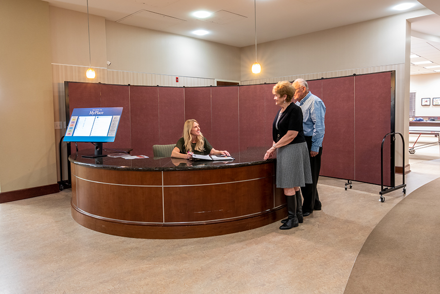Sound absorbing wall behind a woman at a welcome desk talking with an older couple